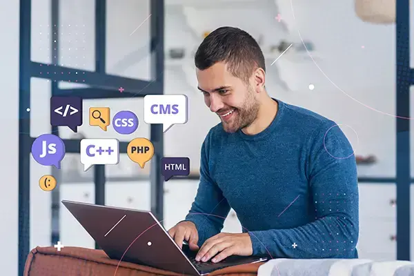 Smiling male web developer programming on a laptop with coding icons floating around him, symbolizing dynamic web development