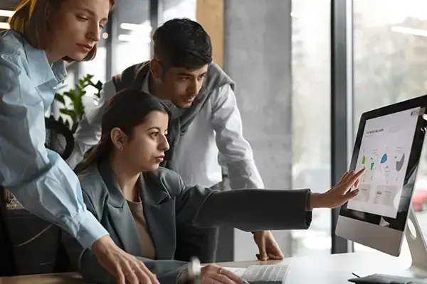 Three professionals analyzing SEO data on a digital screen in a modern office environment, showcasing teamwork and strategy.